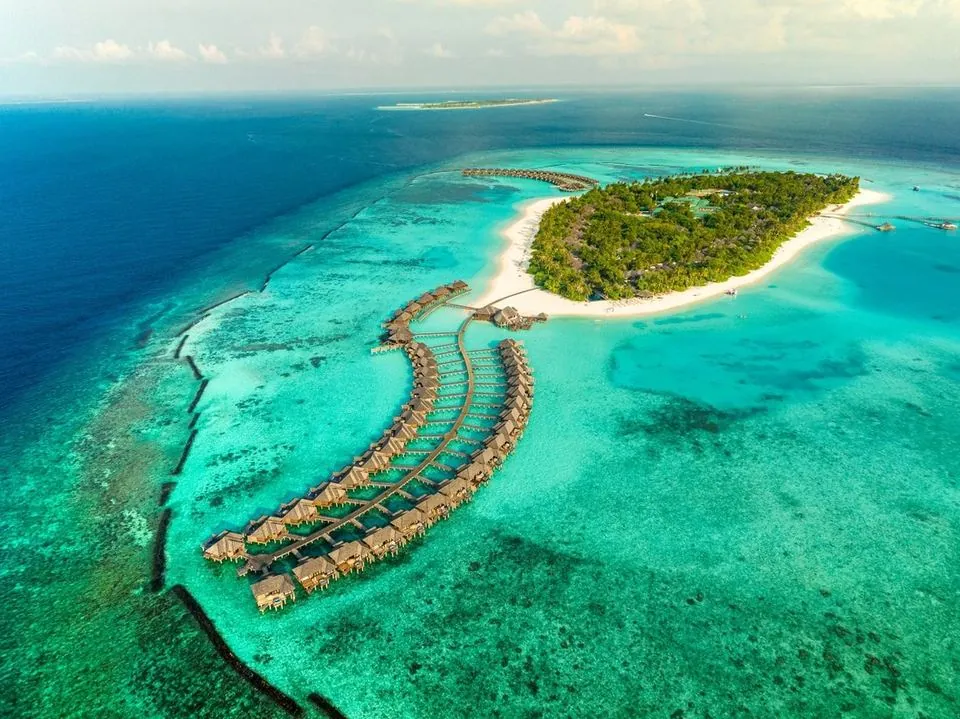 Aerial view of overwater villas curving into a turquoise Maldives lagoon